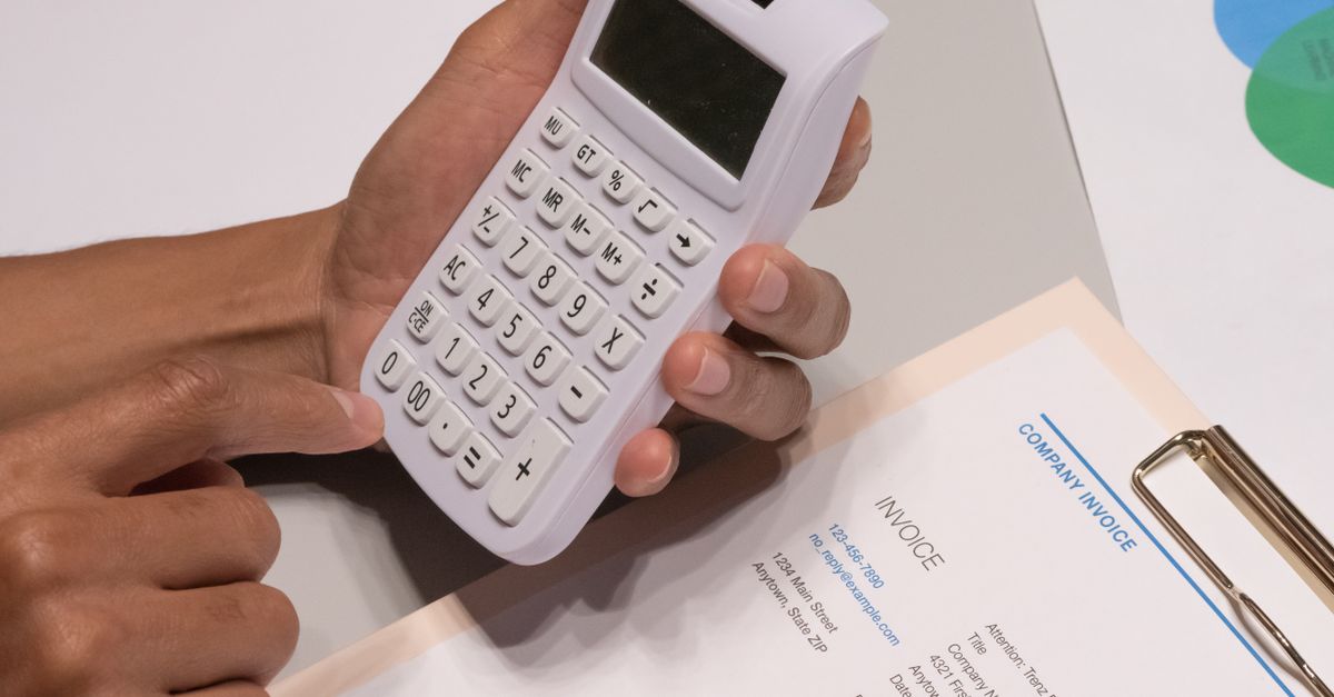 A finance professional reviewing invoices with a calculator at a desk